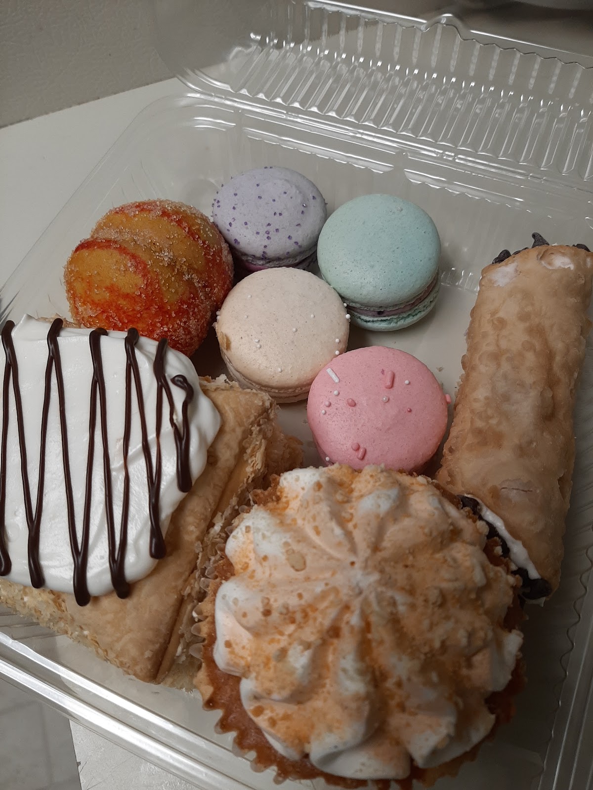 A box of pastel French macarons, a Napoleon slice and cannoli from Aliona's Euro Bake